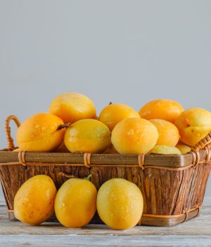 Apricots in a basket on wooden and white gradient background. side view.